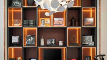 A modern interior with a central round table, two brown chairs, a decorative light fixture, and a bookshelf with various items.
