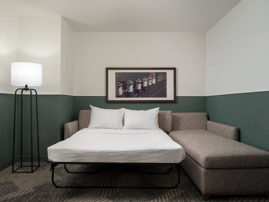 A hotel room with a bed, a floor lamp, and a framed picture on the wall.