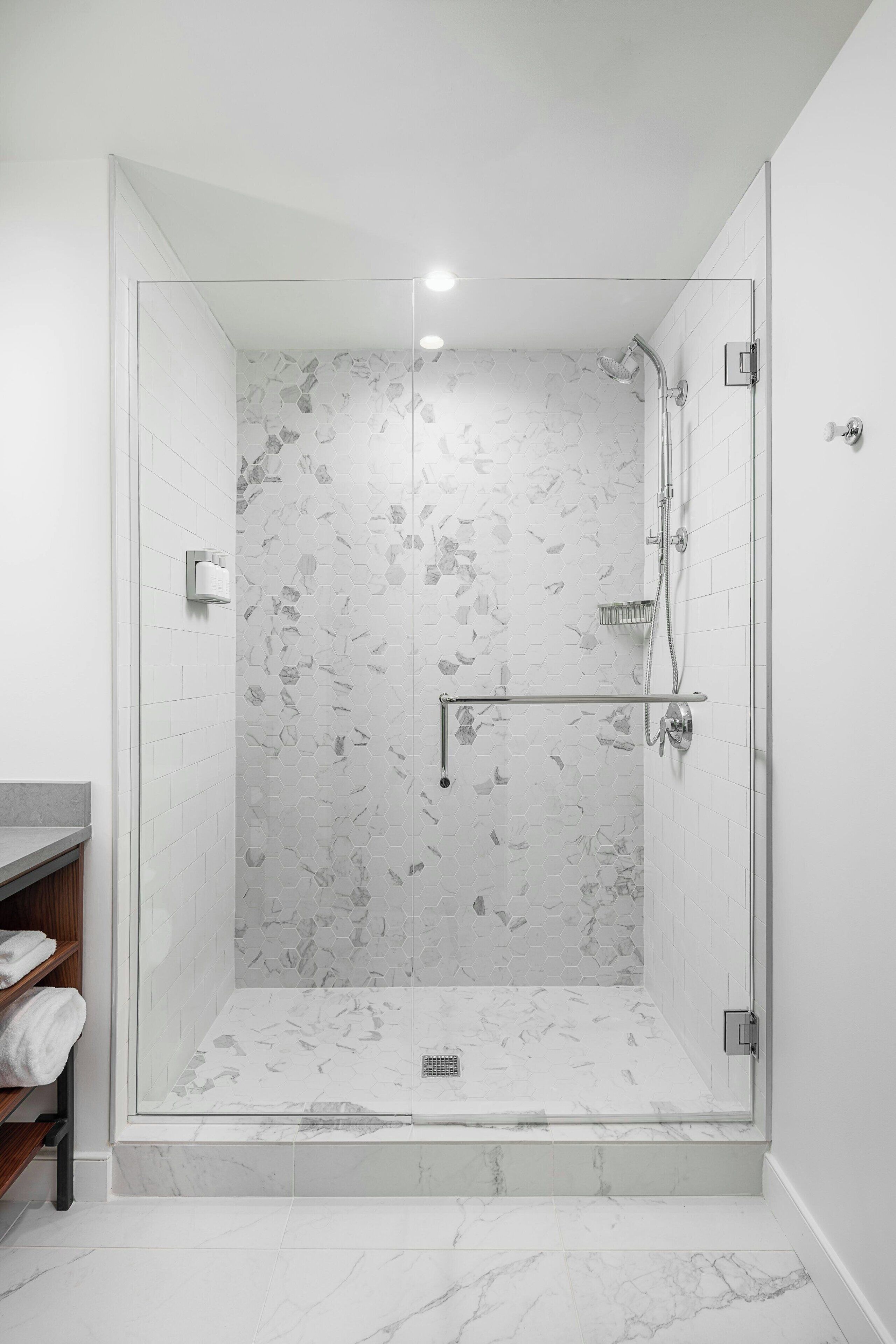 Une douche moderne dotée d’une porte en verre, d’un sol en marbre et d’un mur orné de carreaux hexagonaux.