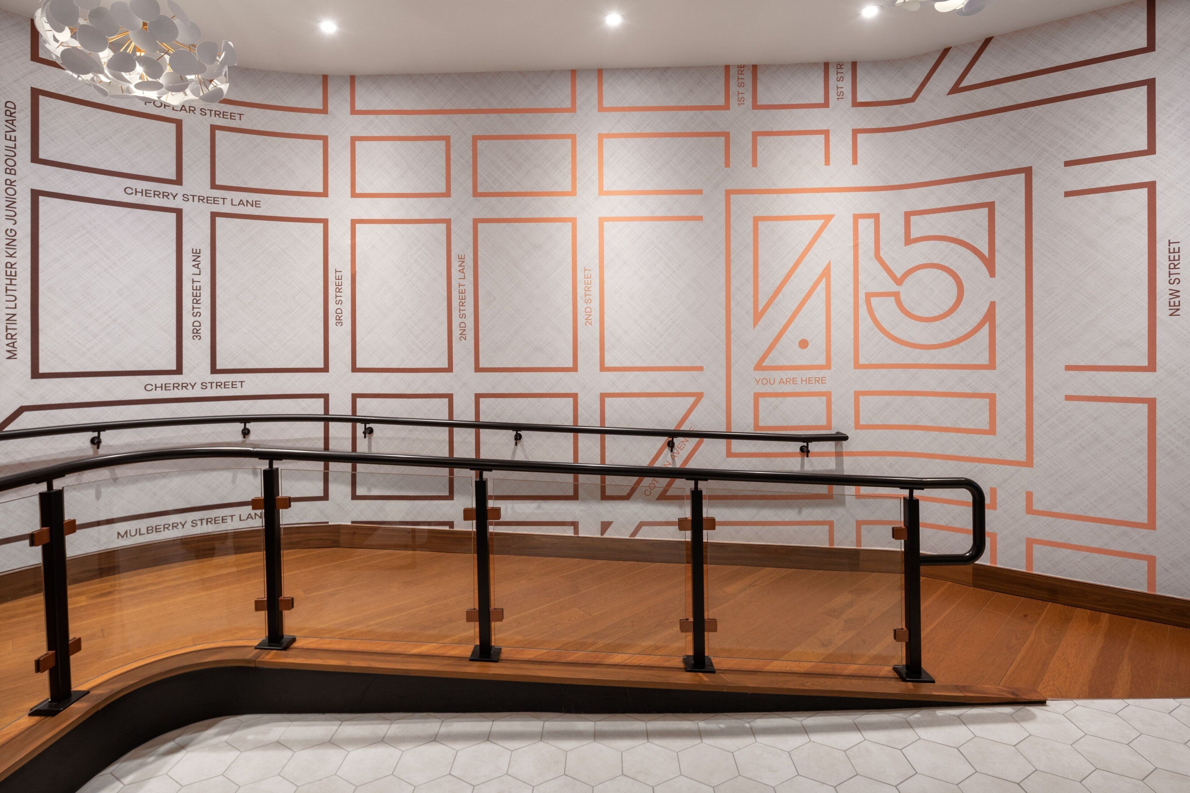 A modern interior with a wooden floor, a black railing, and a wall with street names and a large number '75'.