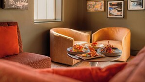 Un salon chaleureux avec deux fauteuils en cuir, une table basse sur laquelle sont disposés des plats, et une grande fenêtre laissant entrer la lumière naturelle.