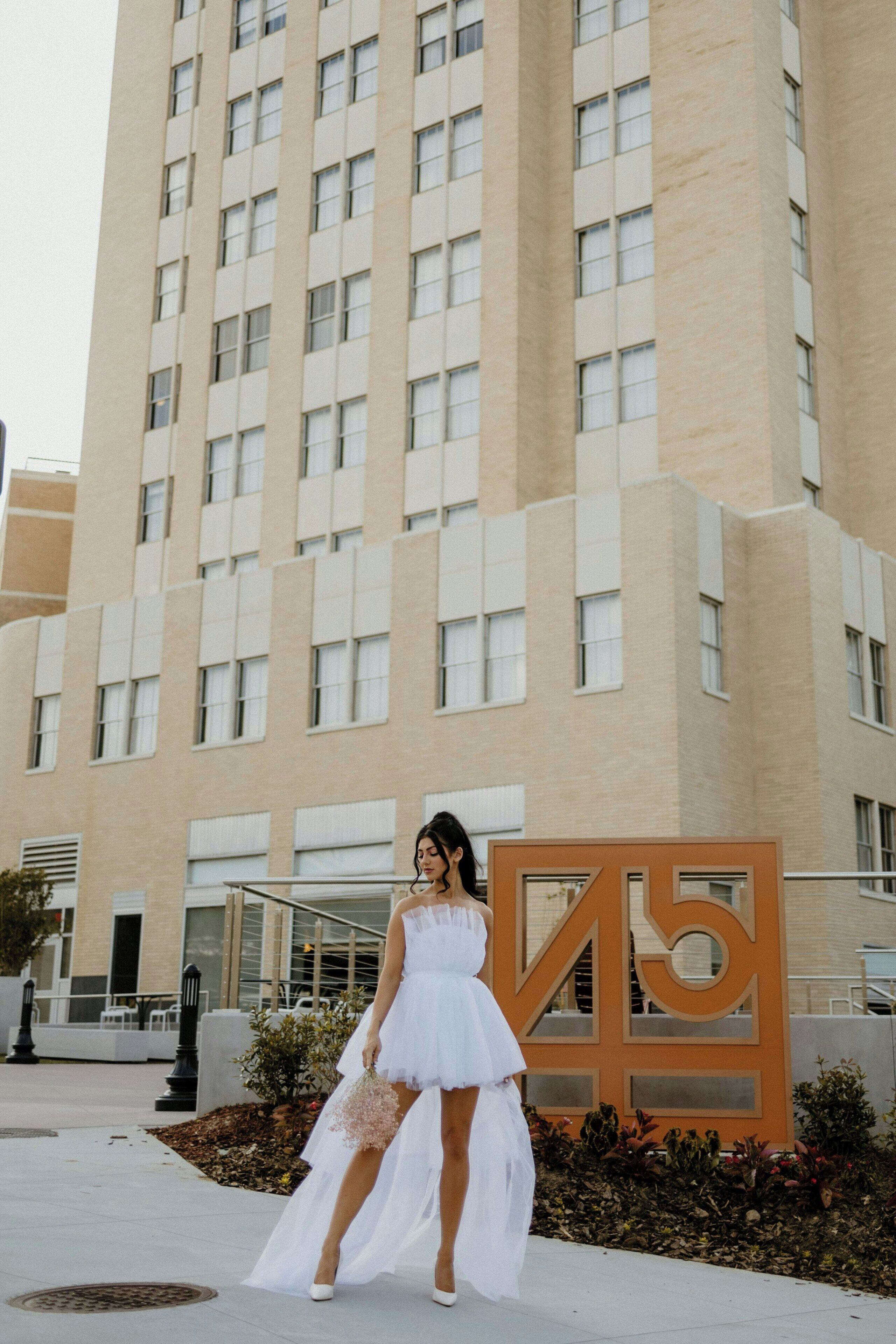 A woman in a white dress standing in front of a building with a large '45' sign.