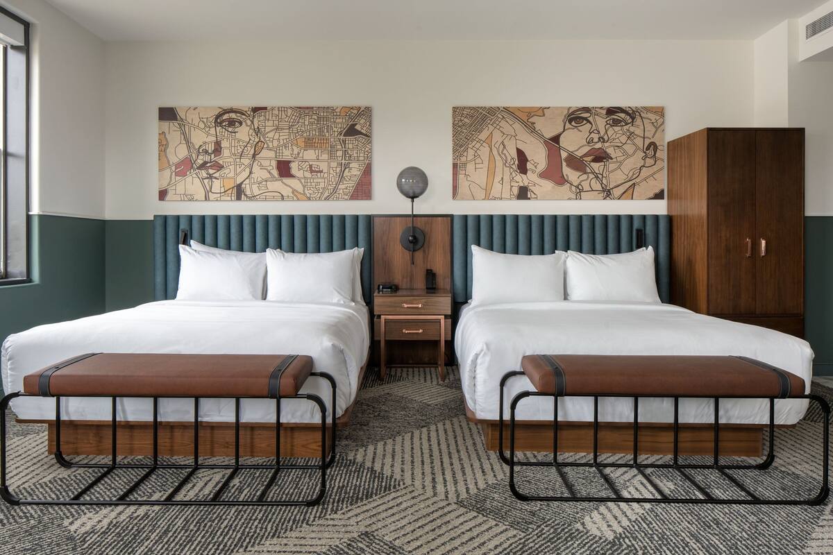 A hotel room with two beds, a wooden wardrobe, a nightstand, and two wall-mounted artworks.