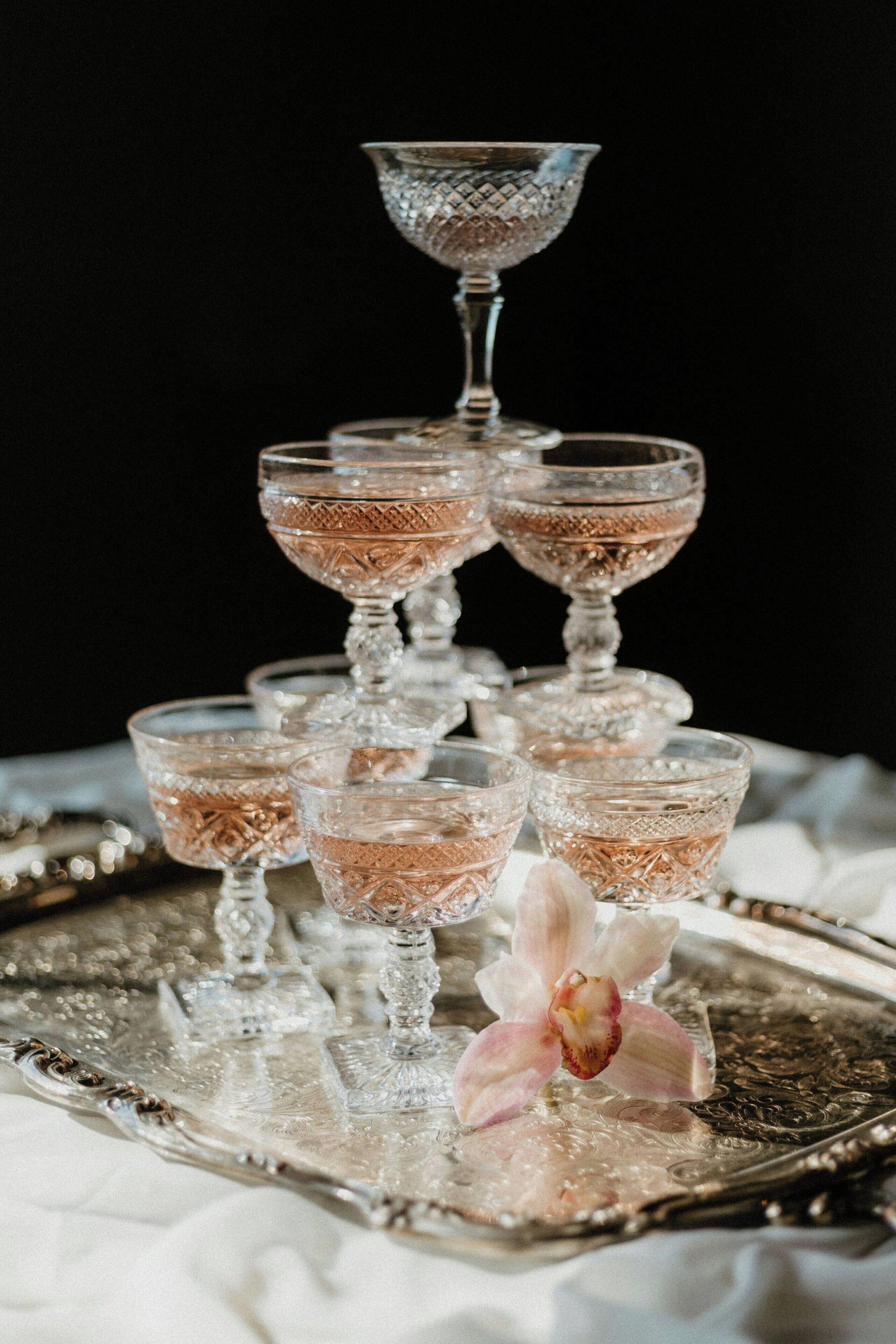 A tiered arrangement of clear glass goblets on a silver tray with intricate designs, accompanied by a single orchid.