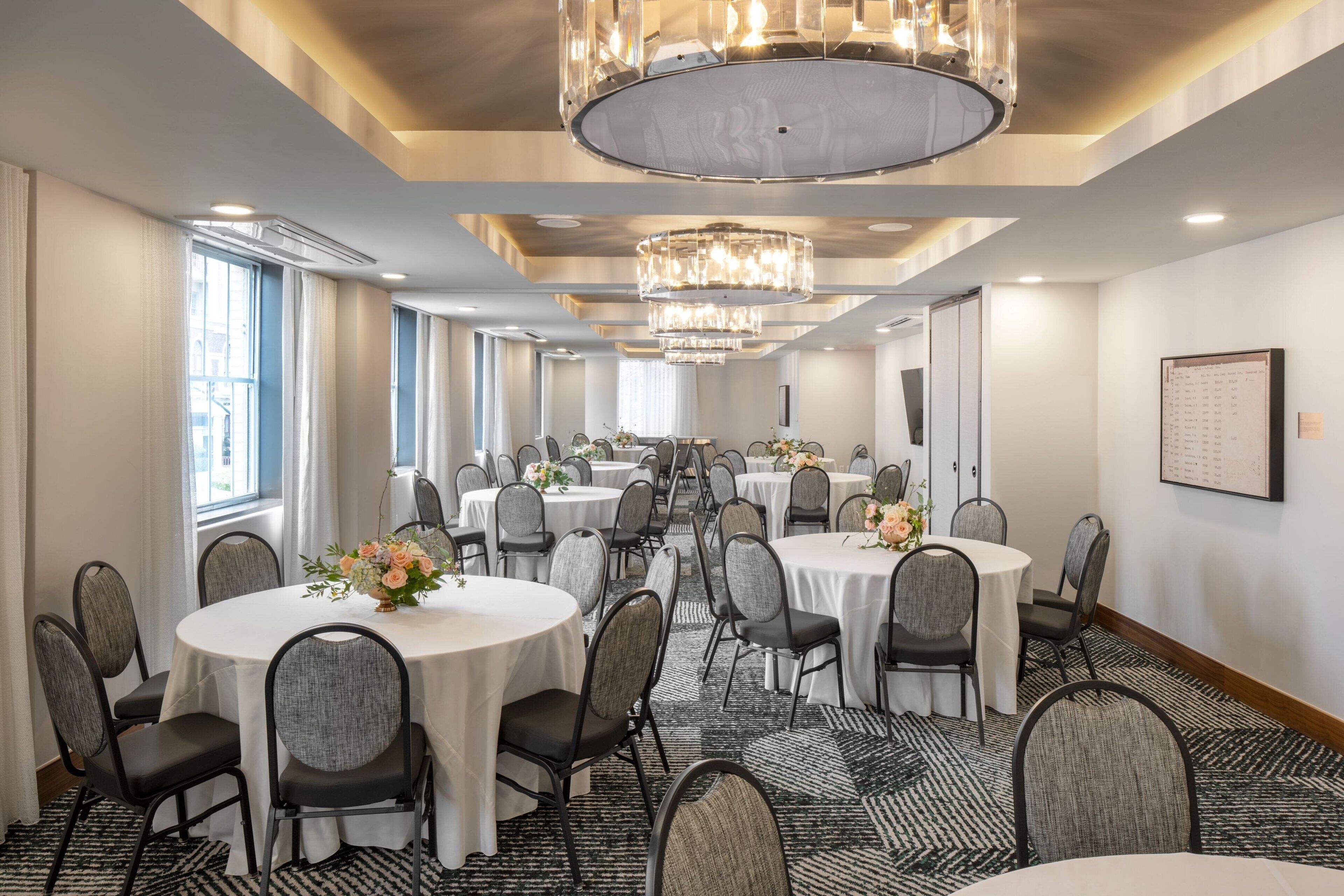 A conference room with multiple round tables, chairs, and chandeliers.