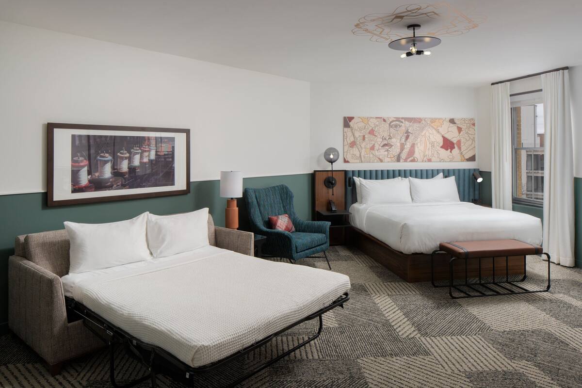 A hotel room with a bed, a chair, a desk, and a large window.