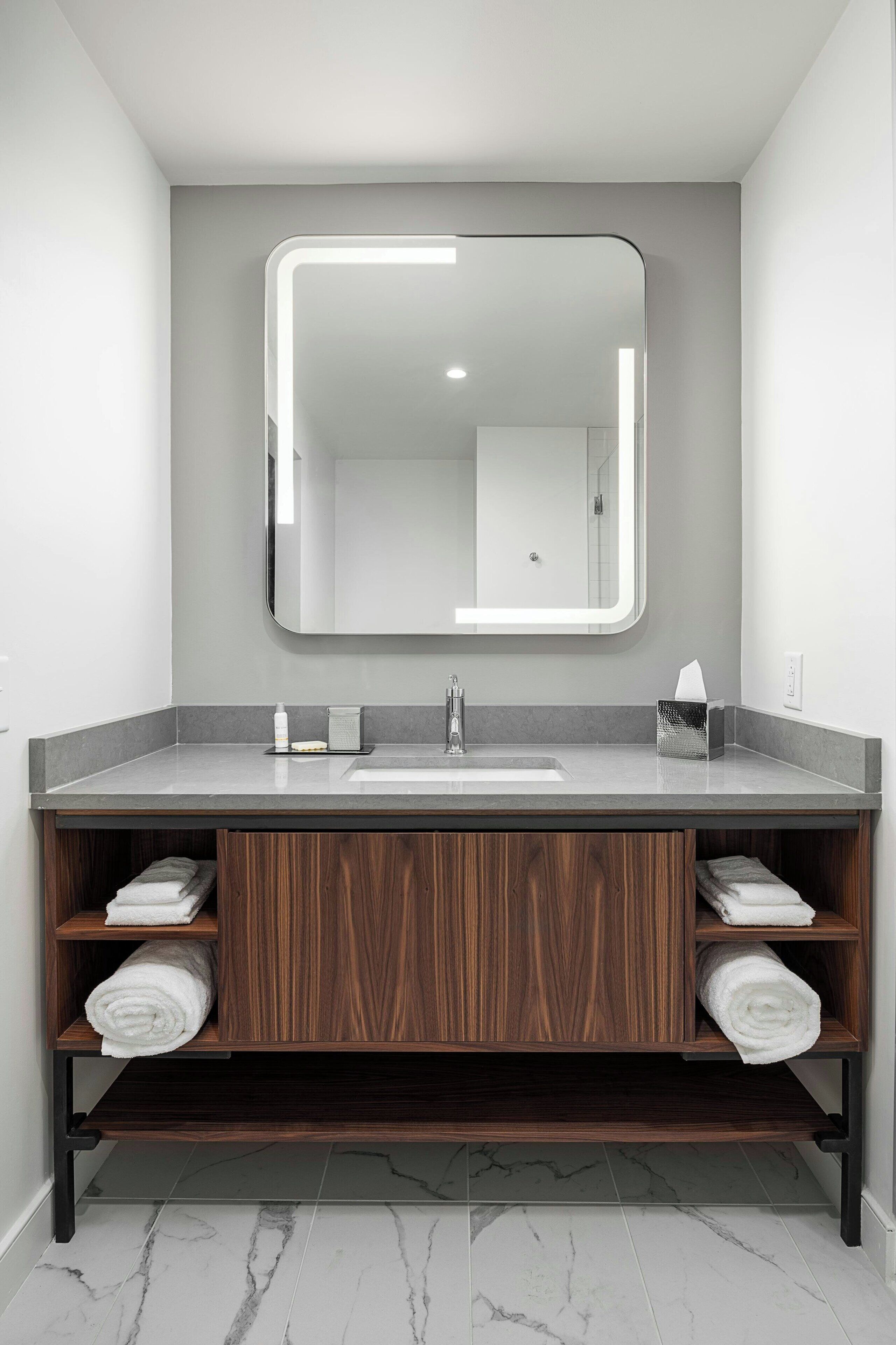 A modern bathroom with a large mirror, a sink, and wooden shelves with towels.