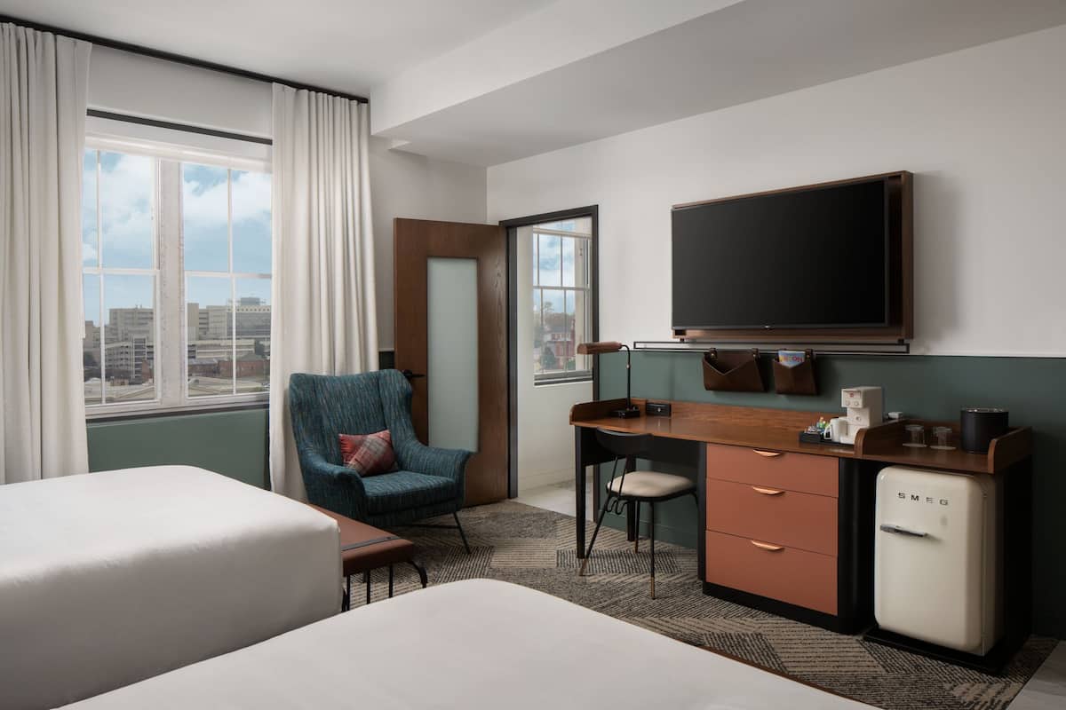 A hotel room with a bed, a desk, a chair, a television, and a minibar.