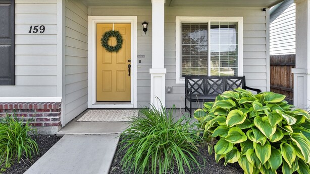 A house with a front door, a number '159' on the wall, a wreath on the door, a bench outside, and a large plant in the front yard. - Sweet as a Peach Family Home (Meridian)