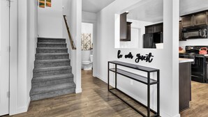 A modern interior with a staircase, a console table with a mirror, and a kitchen area. - Sweet as a Peach Family Home (Meridian)