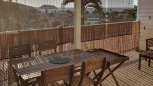 A covered outdoor seating area with a table and chairs, a view of a hilly landscape, and a bamboo fence. - T2 with small pool and beautiful sea view (LES TROIS ILETS)
