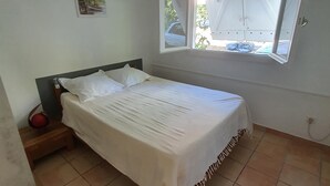 A bedroom with a bed, a ceiling fan, a window with open shutters, and a small picture on the wall. - T2 with small pool and beautiful sea view (LES TROIS ILETS)
