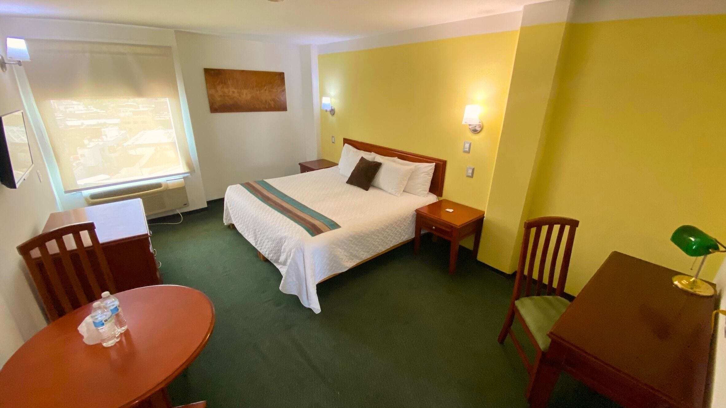 A hotel room with a bed, bedside tables, a desk, a chair, and a window.