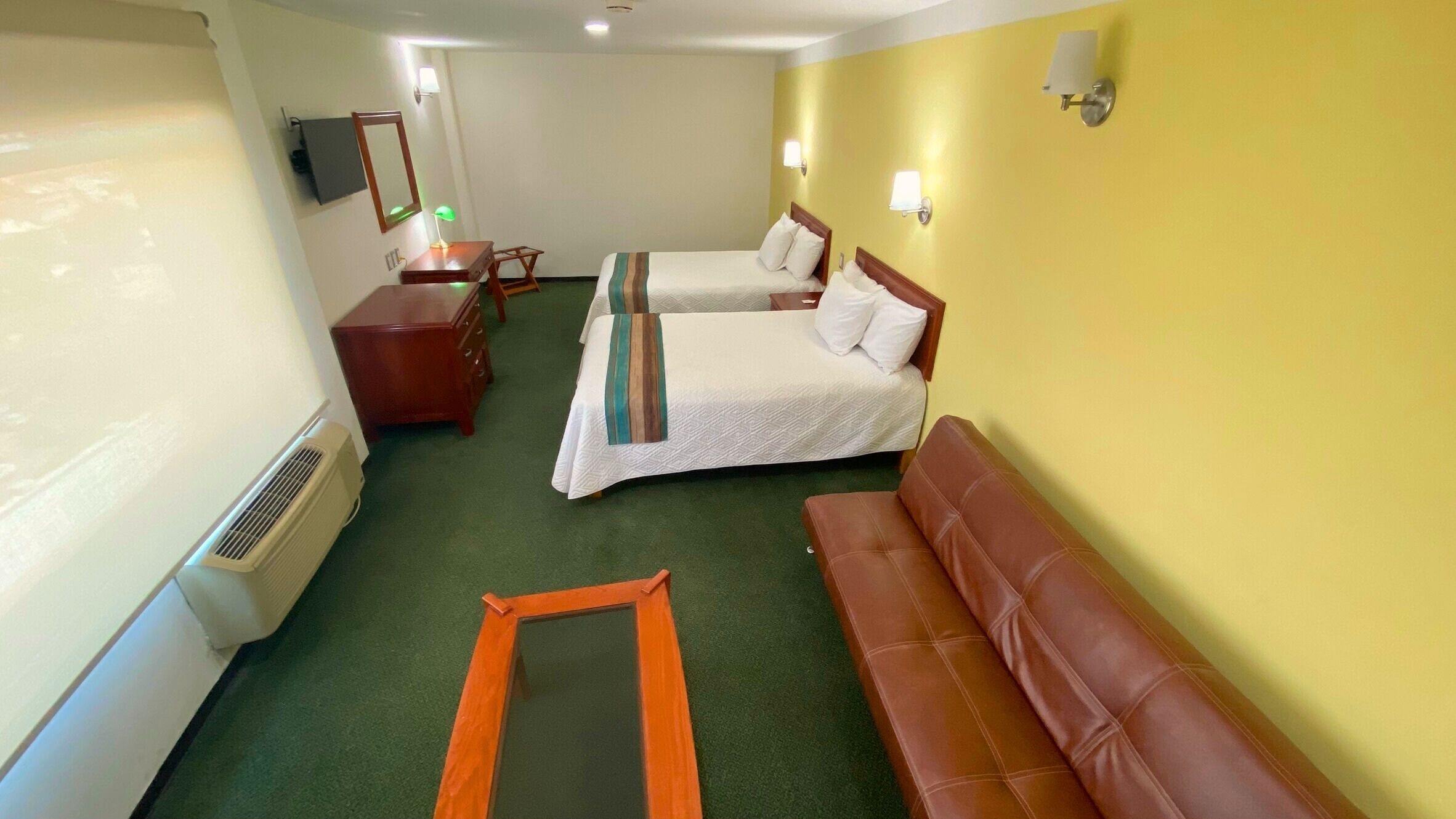 Una habitación de hotel con dos camas, un escritorio, una silla, un sofá y un espejo.