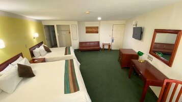 Quarto de hotel com duas camas de solteiro, um sofá, uma mesa de trabalho, uma cadeira e uma televisão.