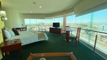 Een hotelkamer met een bed, een bureau, een televisie en uitzicht op een stadsgezicht door grote ramen.