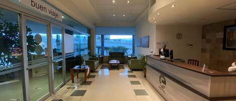 Een hotel lobby met een receptiebalie, een zithoek en een glazen wand met uitzicht.