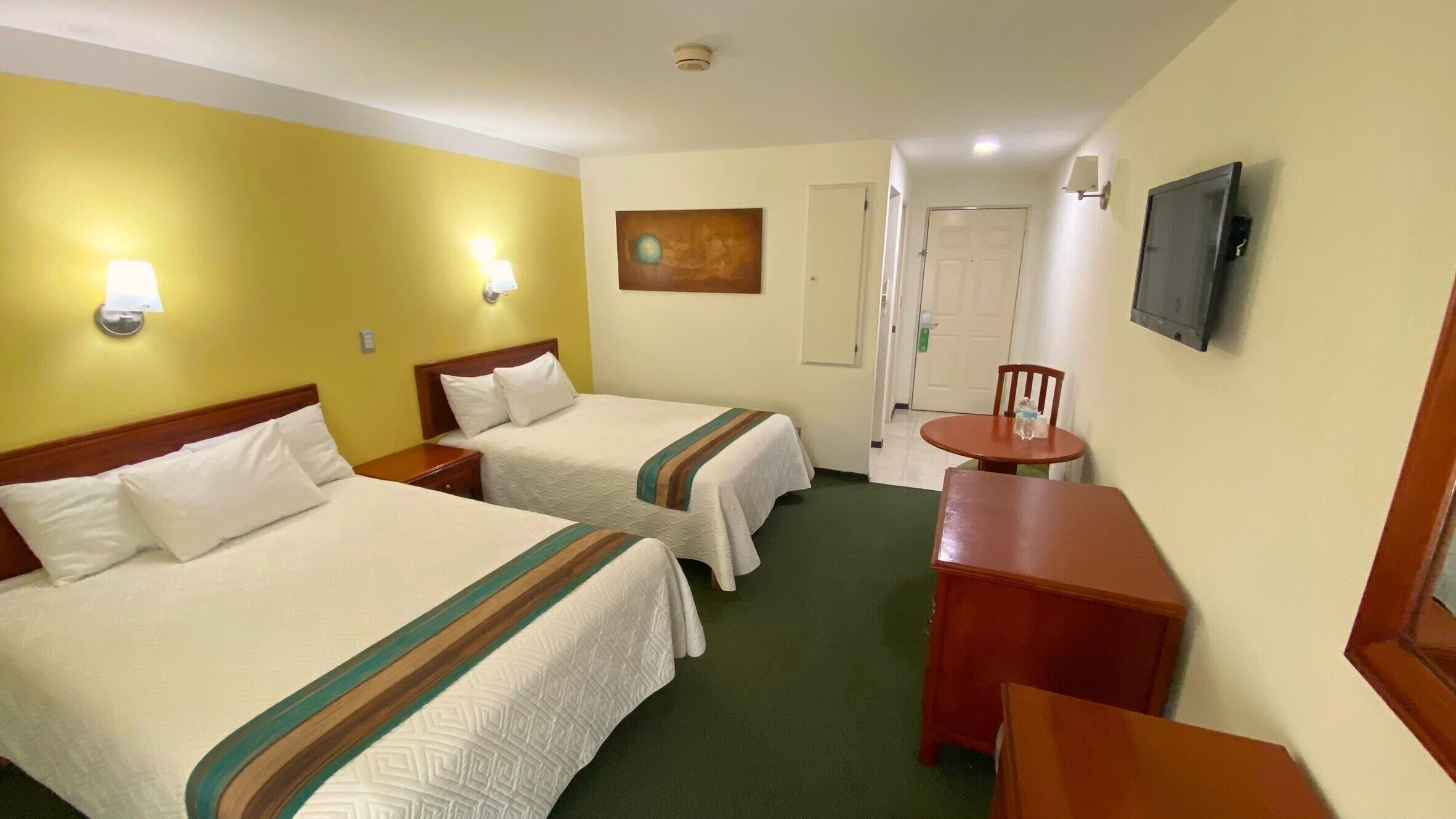 A hotel room with two beds, a small table, a chair, a TV, and a painting on the wall.