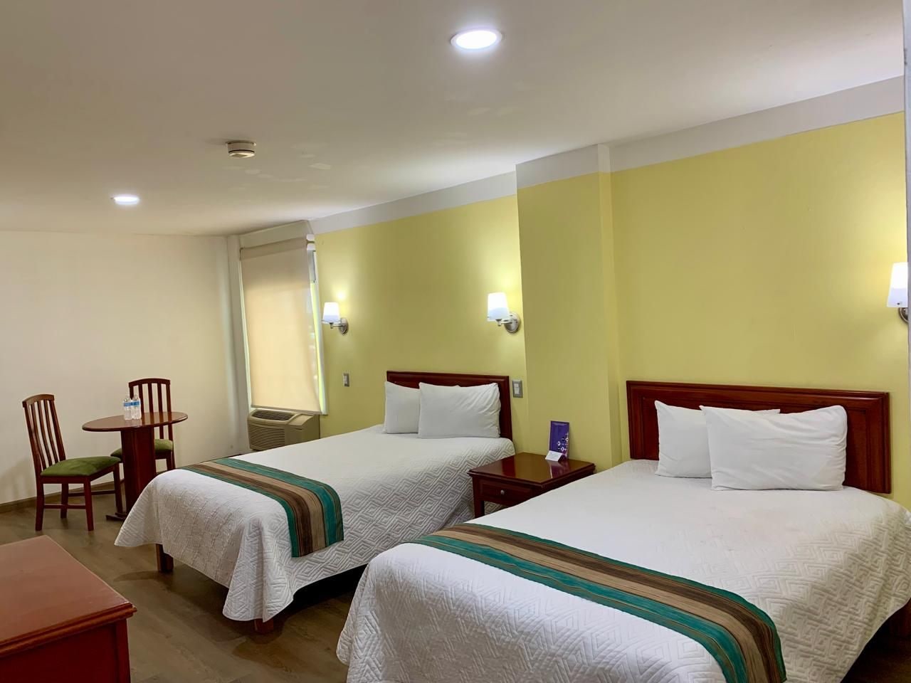 A hotel room with two beds, a small table with chairs, and a desk.