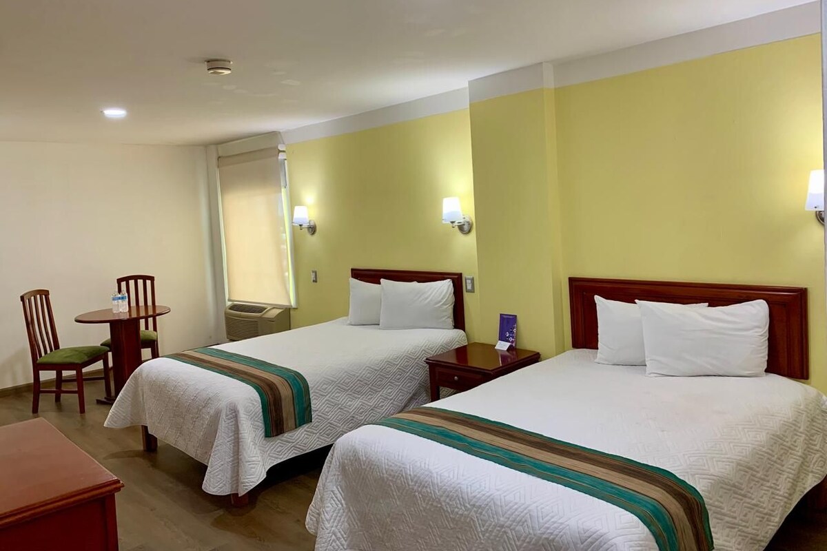 Una camera d'albergo con due letti, un piccolo tavolo con sedie e una scrivania.