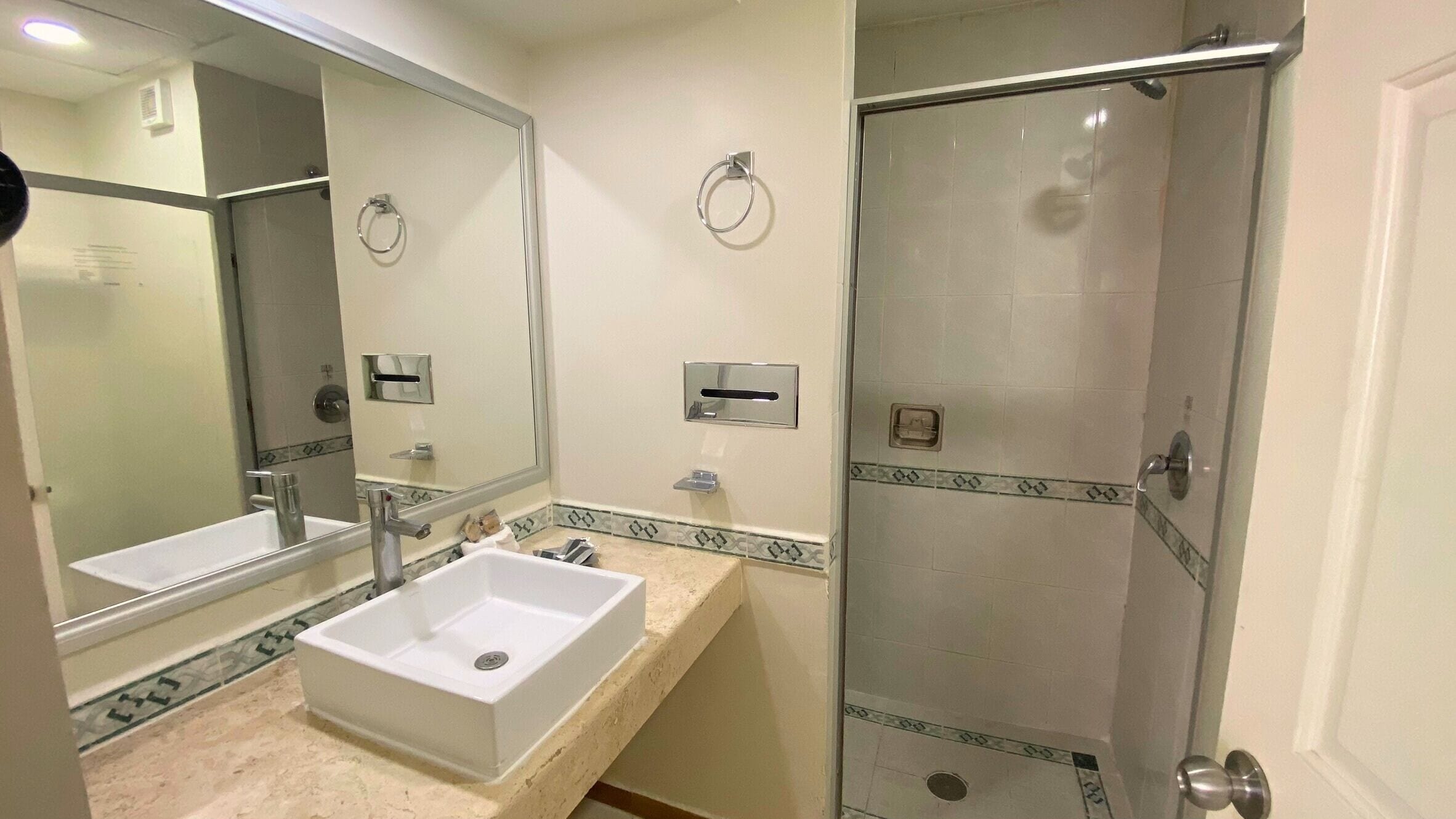 A bathroom with a large mirror, a sink, and a glass-enclosed shower.