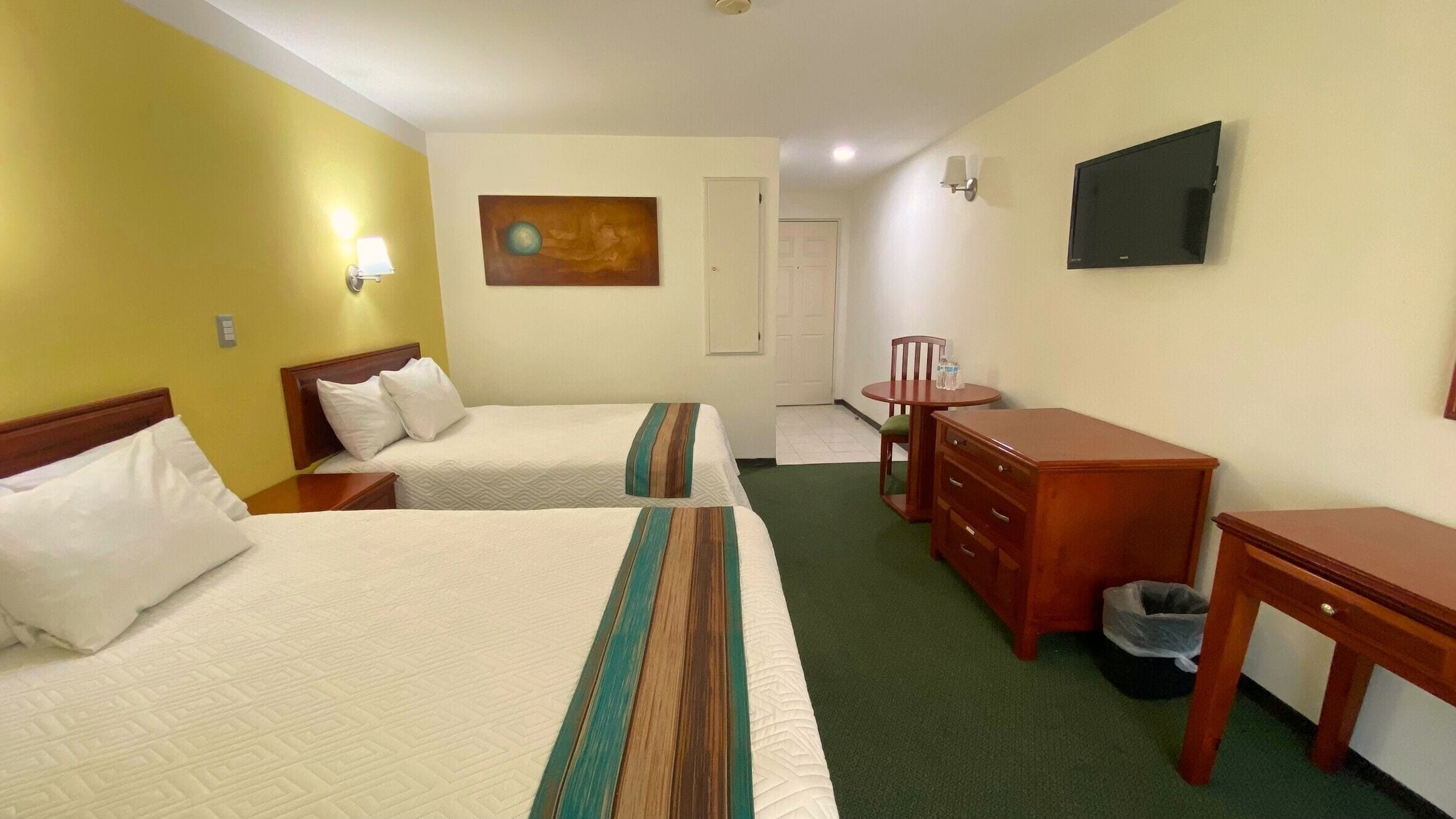 A hotel room with two beds, a desk, a chair, a TV, and a painting on the wall.