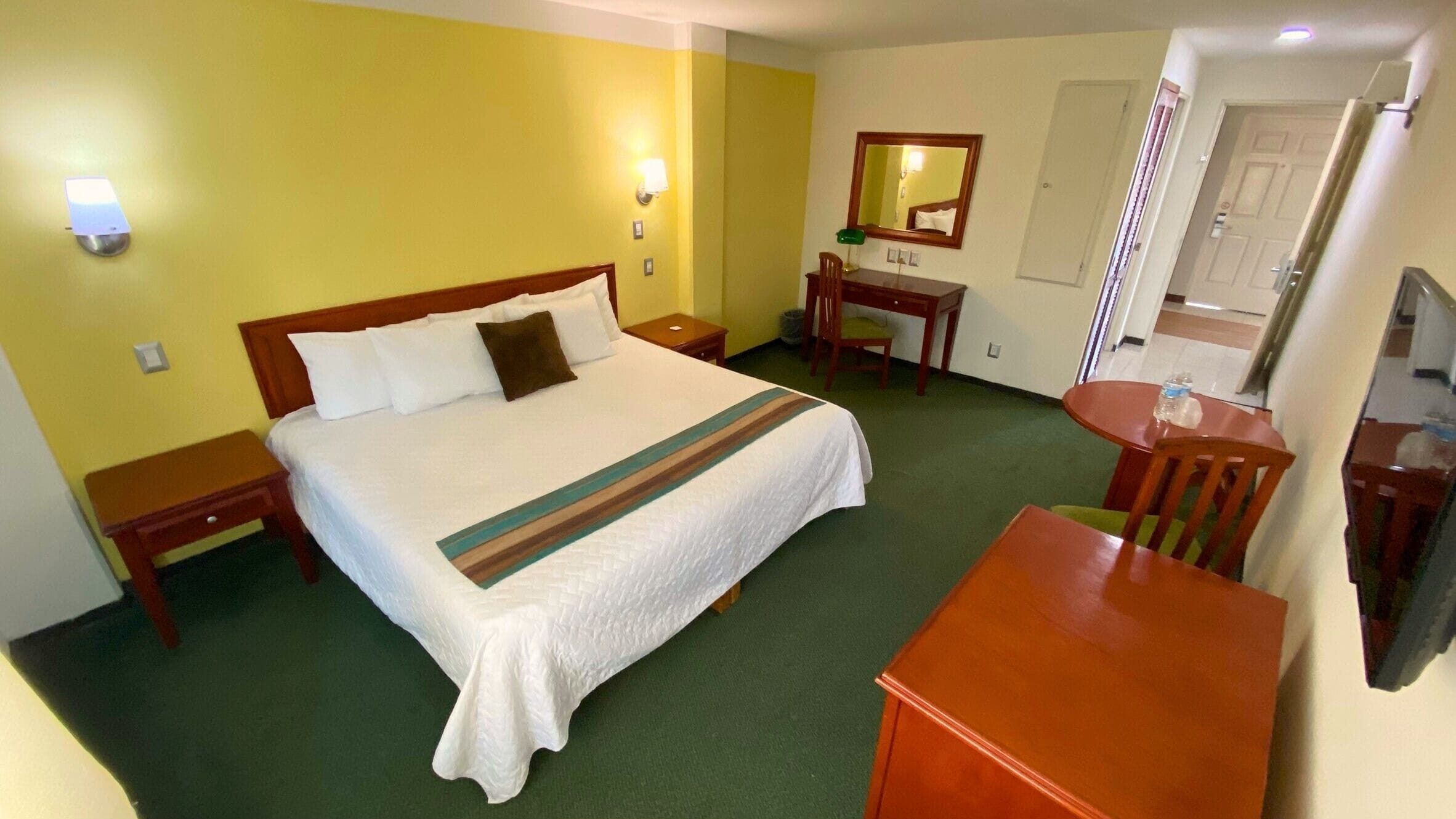 Une chambre d’hôtel comprenant un lit, des tables de chevet, un bureau, une chaise, un miroir et un téléviseur.