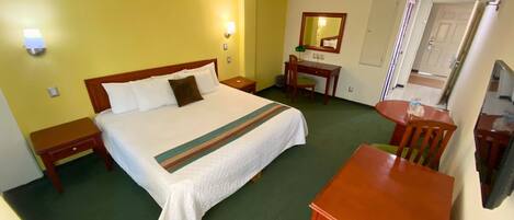 Une chambre d’hôtel comprenant un lit, des tables de chevet, un bureau, une chaise, un miroir et un téléviseur.