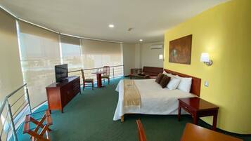 Habitación de hotel con cama, escritorio, silla, televisor y balcón con vistas.