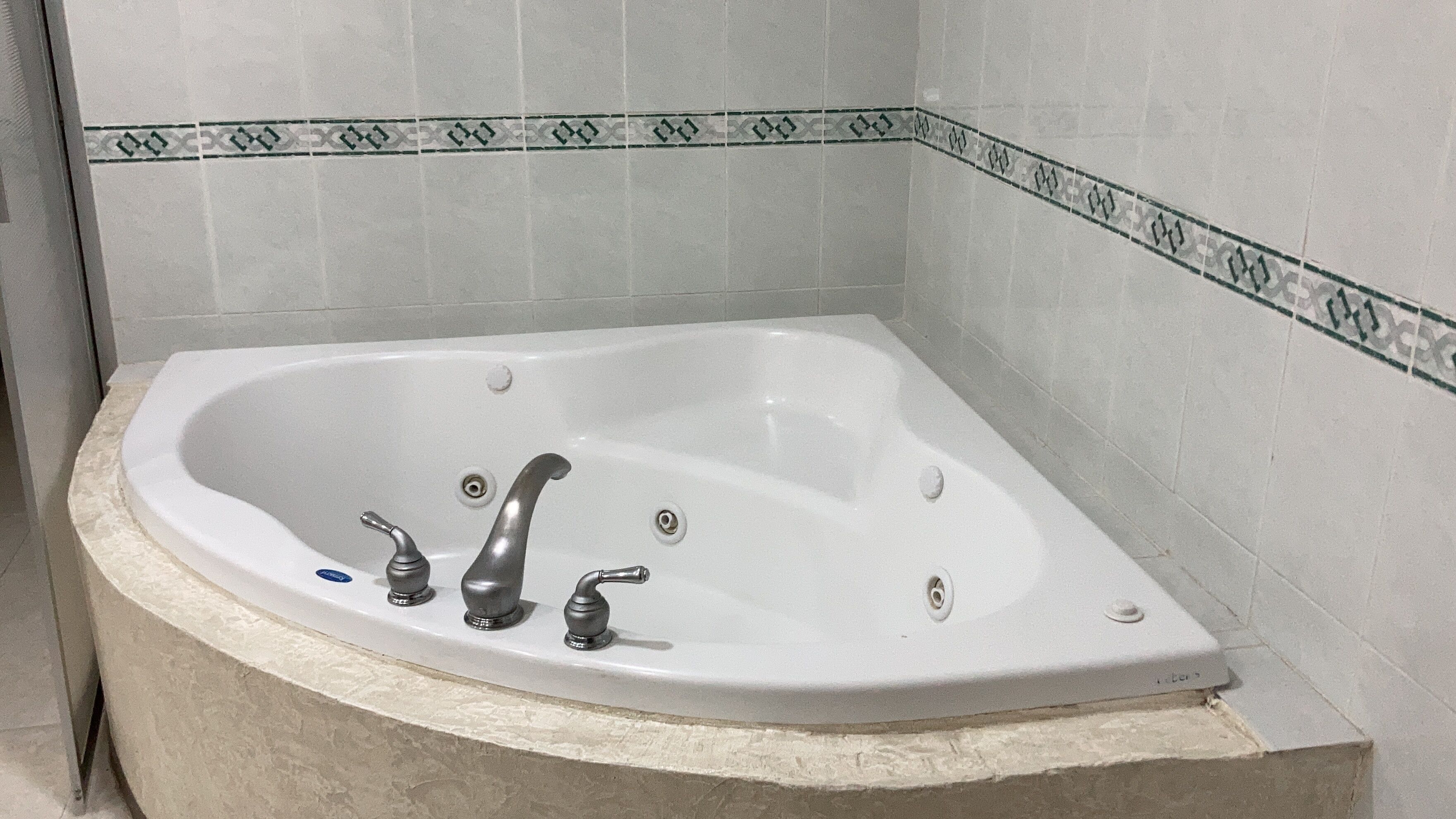 A corner bathtub with two faucets and a drain.
