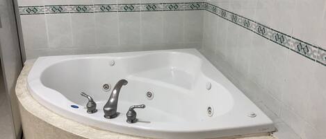A corner bathtub with two faucets and a drain.