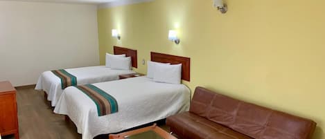 A hotel room with two single beds, a brown leather sofa, a wooden coffee table, and a small wooden side table.
