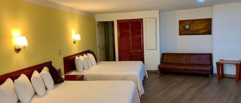Quarto de hotel com duas camas, um sofá, uma mesa pequena e um quadro na parede.