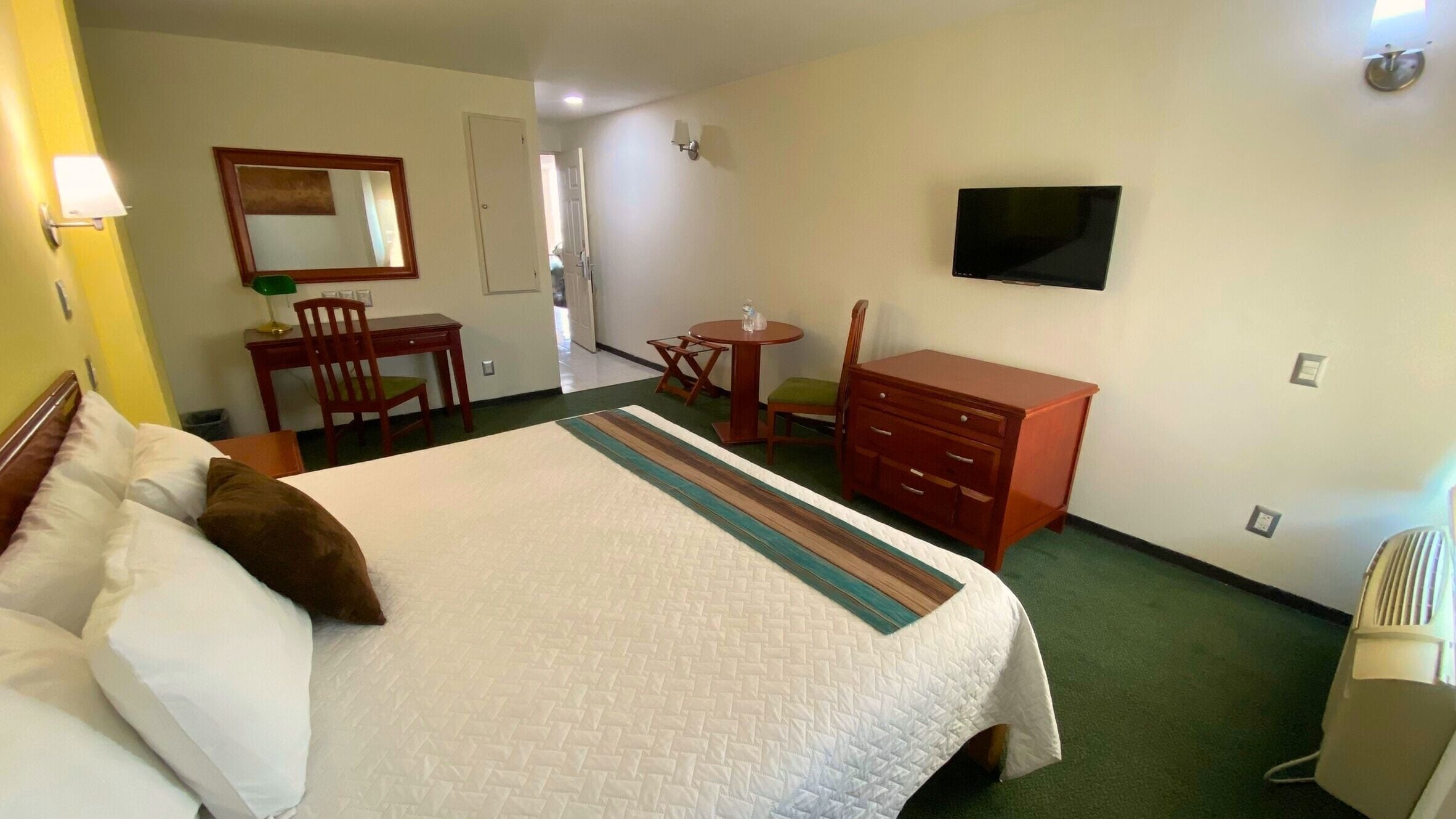 Habitación de hotel con cama, escritorio, silla, cómoda, televisor y una pequeña mesa con una silla.