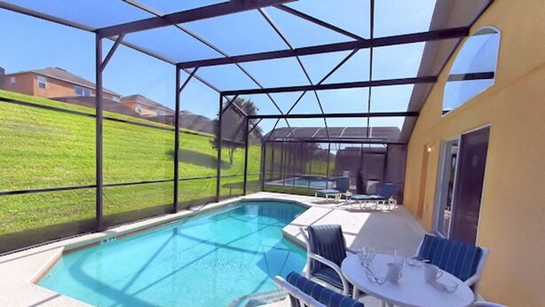 A covered outdoor swimming pool with lounge chairs and a table, surrounded by a safety fence. - Emerald Pleasure Villa - Private Pool, Resort Community, Near Disney (Kissimmee)