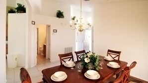 A dining area with a wooden table set for four, surrounded by chairs. There is a chandelier hanging from the ceiling, and the walls are white. - Emerald Pleasure Villa - Private Pool, Resort Community, Near Disney (Kissimmee)