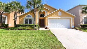 A two-story house with a garage, palm trees, and a well-maintained lawn. - Emerald Pleasure Villa - Private Pool, Resort Community, Near Disney (Kissimmee)
