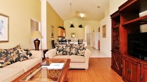A living room with a sofa, coffee table, and TV stand. There is a dining area with a table and chairs in the background. - Emerald Pleasure Villa - Private Pool, Resort Community, Near Disney (Kissimmee)