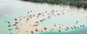 An aerial view of a beach with numerous boats anchored in the water and people on the sand.