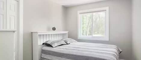 A bedroom with a bed, a window, and a door.