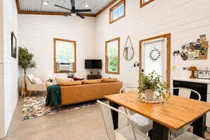 A cozy living room with a sofa, a dining table, and a TV. - Free Pumpkin Patch Tickets + Farm Stay (Spring Branch)