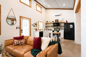 A cozy living room with a leather sofa, a dining table with chairs, and a kitchen area with a refrigerator and microwave. - Free Pumpkin Patch Tickets + Farm Stay (Spring Branch)