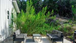 An outdoor patio with two grey sofas and a small table, surrounded by dense green foliage. - Spring Break | Hot Tub, Pool, Farm Stay (Spring Branch)
