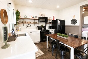 Een moderne keuken met witte kasten, een houten eettafel, zwarte stoelen, een zwarte koelkast en een magnetron.