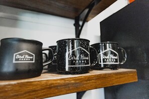 Trois tasses noires ornées du logo « Bird Haus Farms », posées sur une étagère en bois.