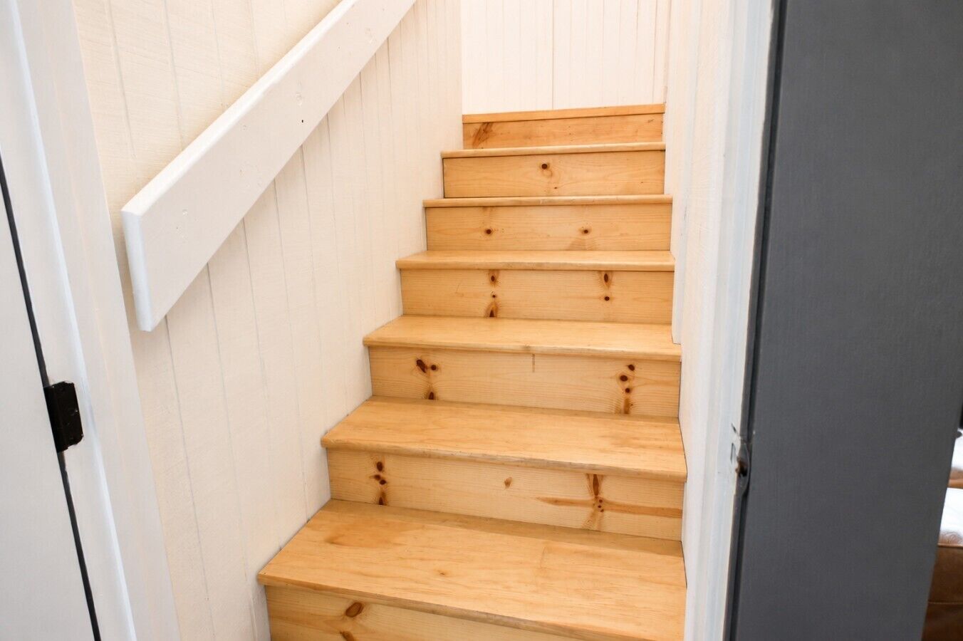 A wooden staircase with white walls and a gray door.