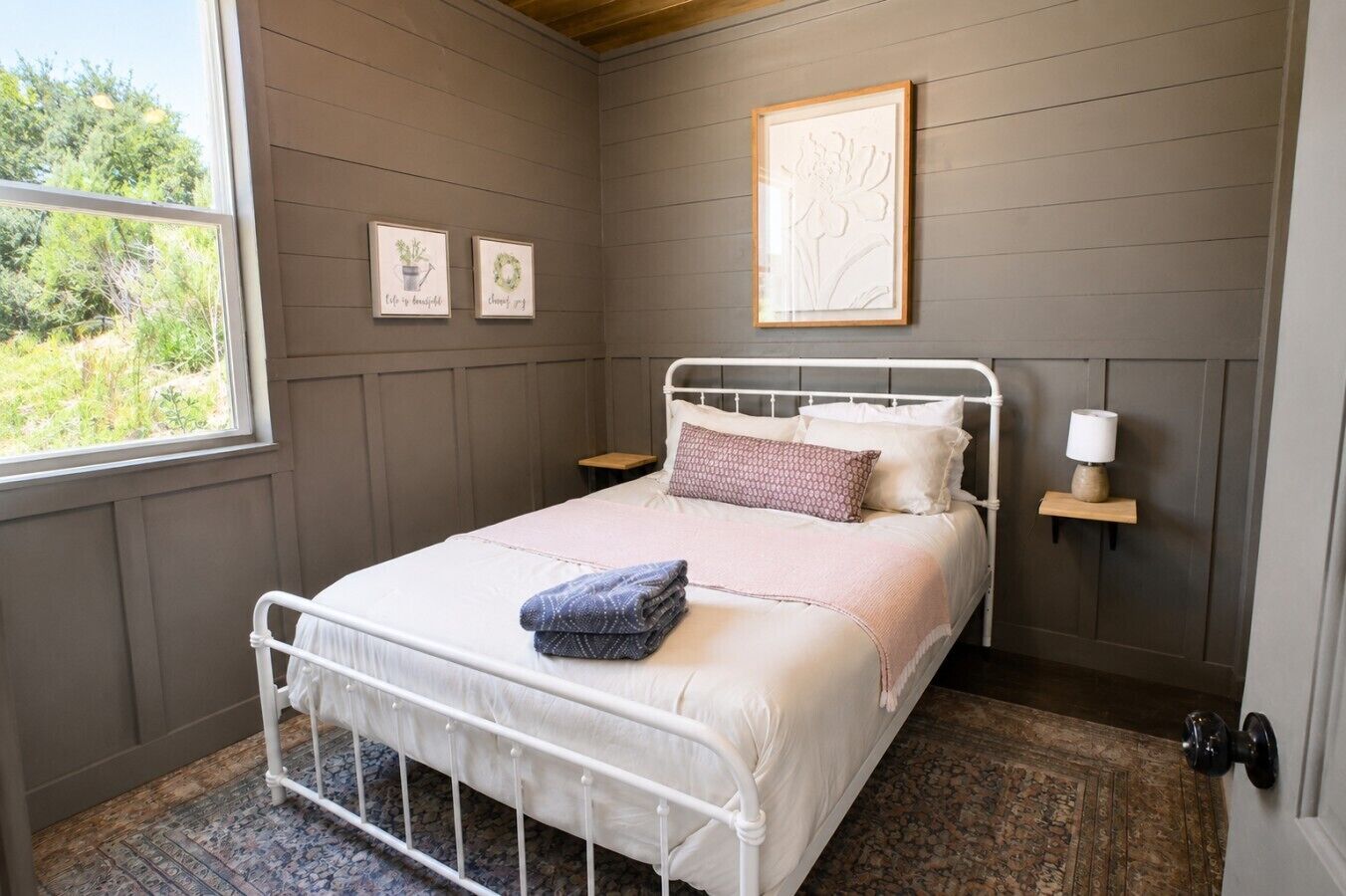 Une chambre à coucher comprenant un lit, des tables de chevet, une fenêtre et des œuvres d’art accrochées au mur.