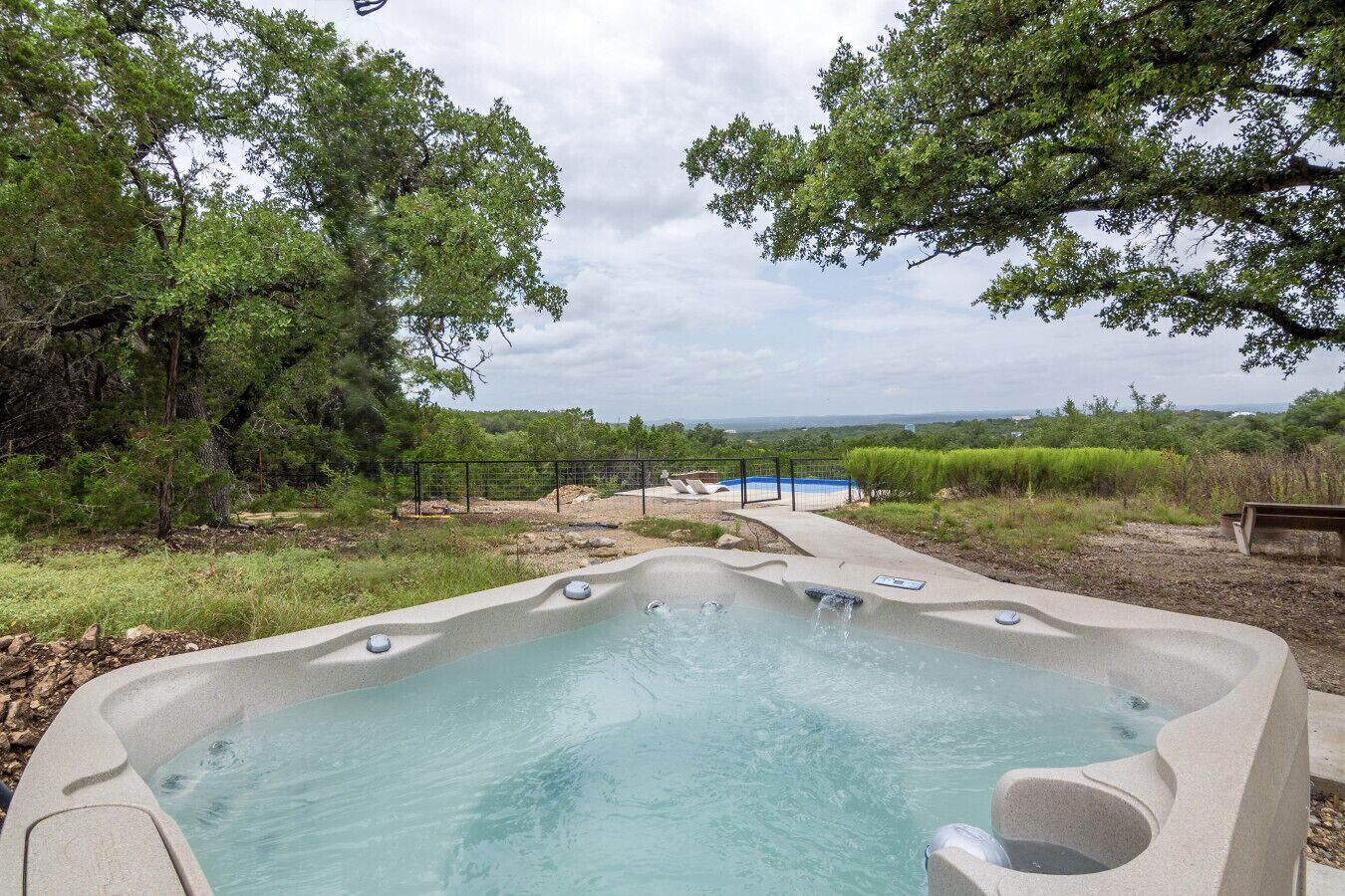 Un bain à remous entouré d’arbres et une piscine clôturée.