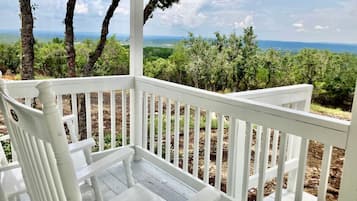 Eine weiße Holzdielen-Terrasse mit Blick auf einen Wald und entfernte Berge.