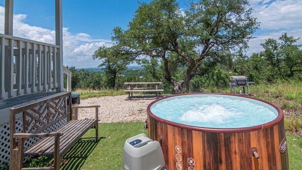 A wooden hot tub with a view of a tree and a picnic table in a grassy area. - Summer Escape with Swim Hole and Golf Cart Rental (Spring Branch)